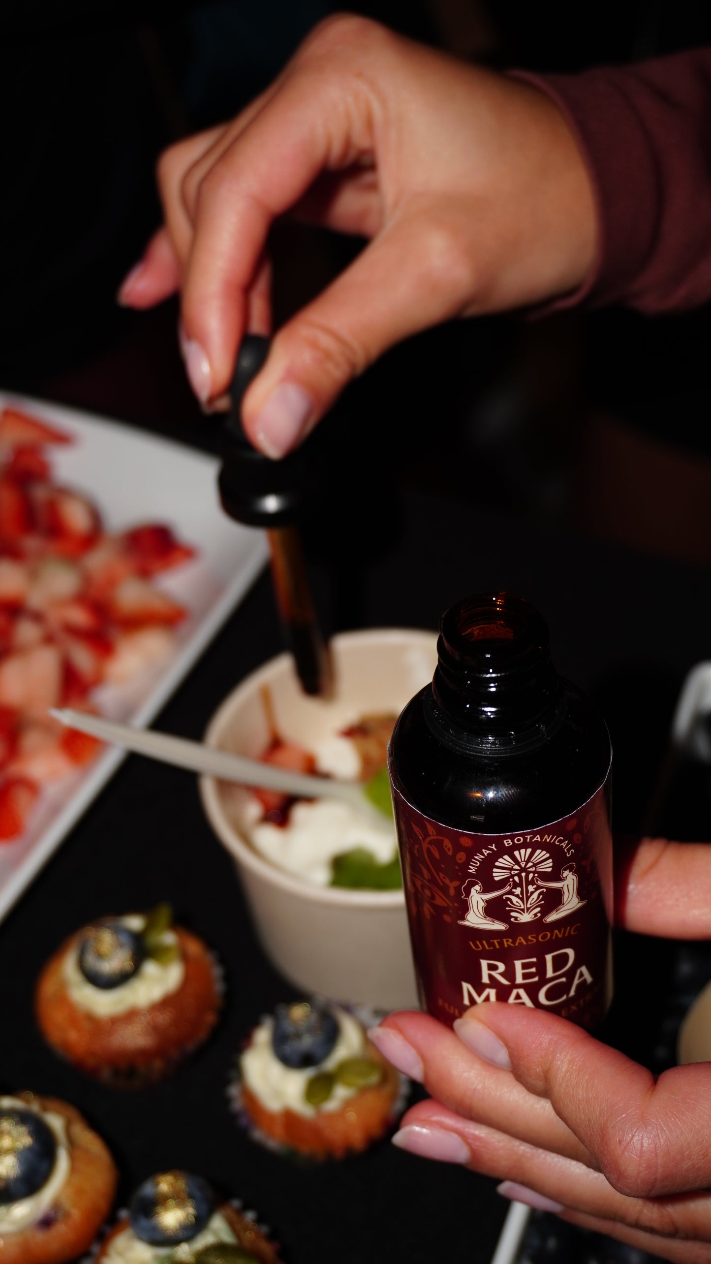 Hands pouring or serving a Red Maca drink with fresh ingredients on a rustic table.